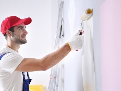Young worker painting wall in room